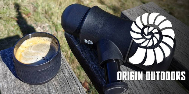 Origin Outdoors 'To-Go' Mini-Espresso Maker on a wooden surface with a blurred natural background and 'Origin Outdoors' logo.
